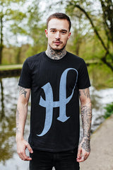 Man in a black direction t-shirt featuring a large blue letter H
