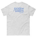 Light gray sunsets t-shirt with blue print ’SUCKER for SUNSETS’ on back